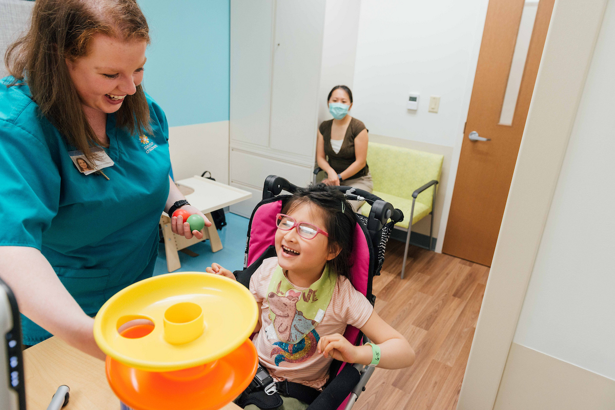Young girl in a wheelchair has fun in outpatient rehabilitation visit with mom and caregiver.