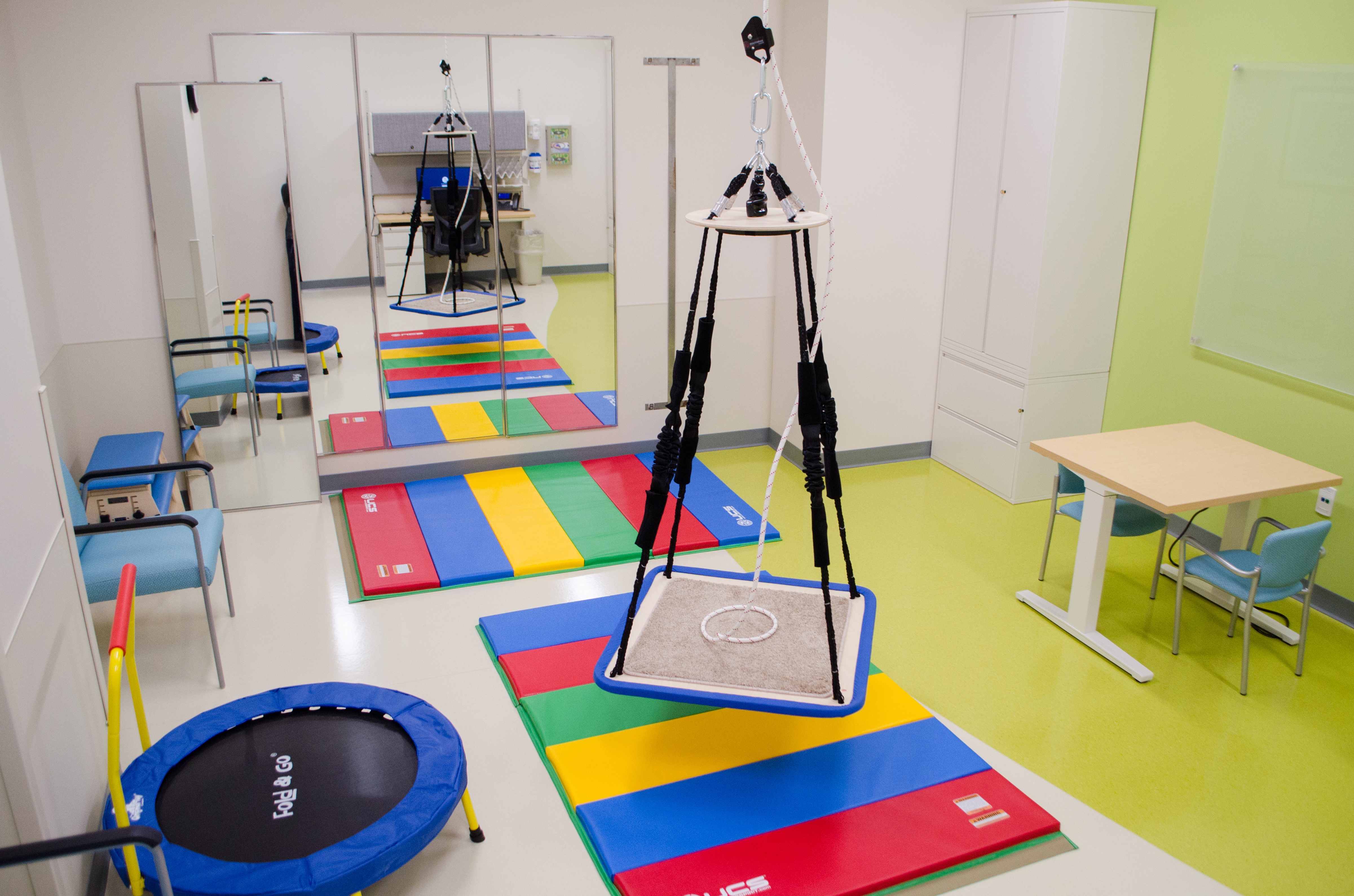 Large rehab room with tables for therapy with sports theme art designs on wall.